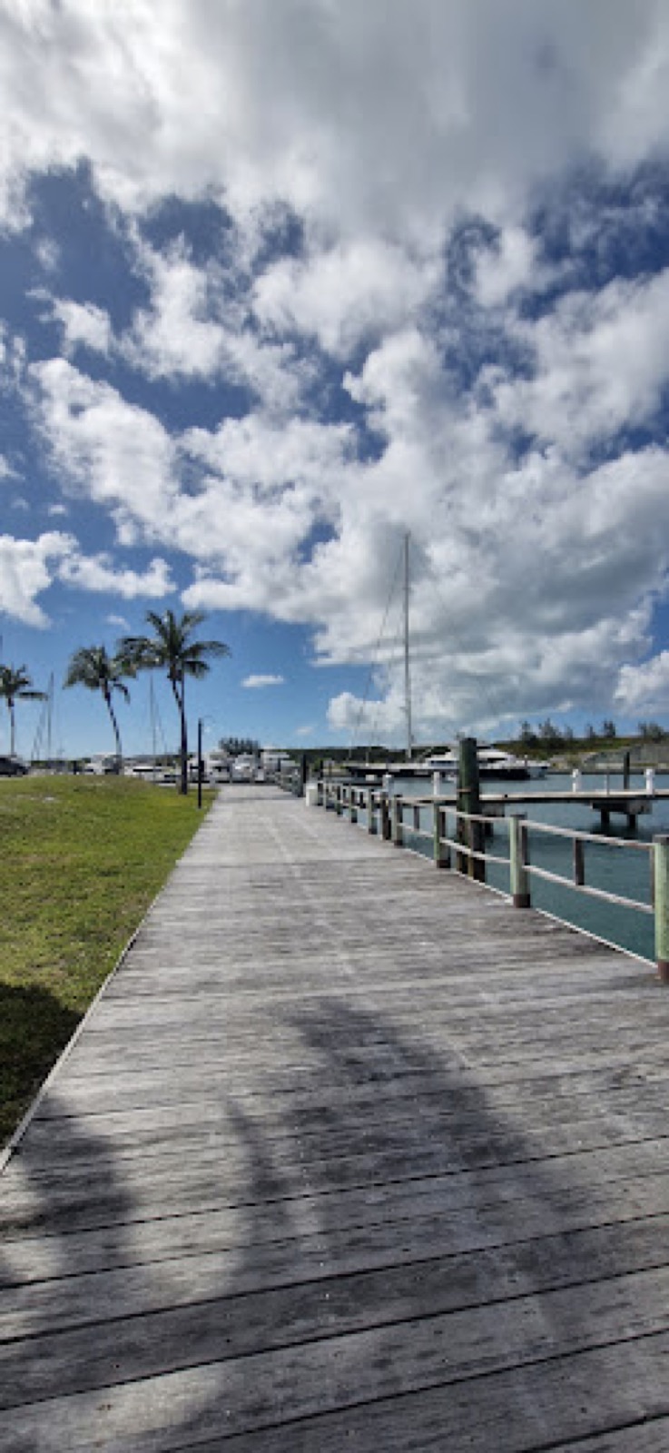 Wooden boardwalk beside a marina dock with sailboats under a cloudy Bahamian sky