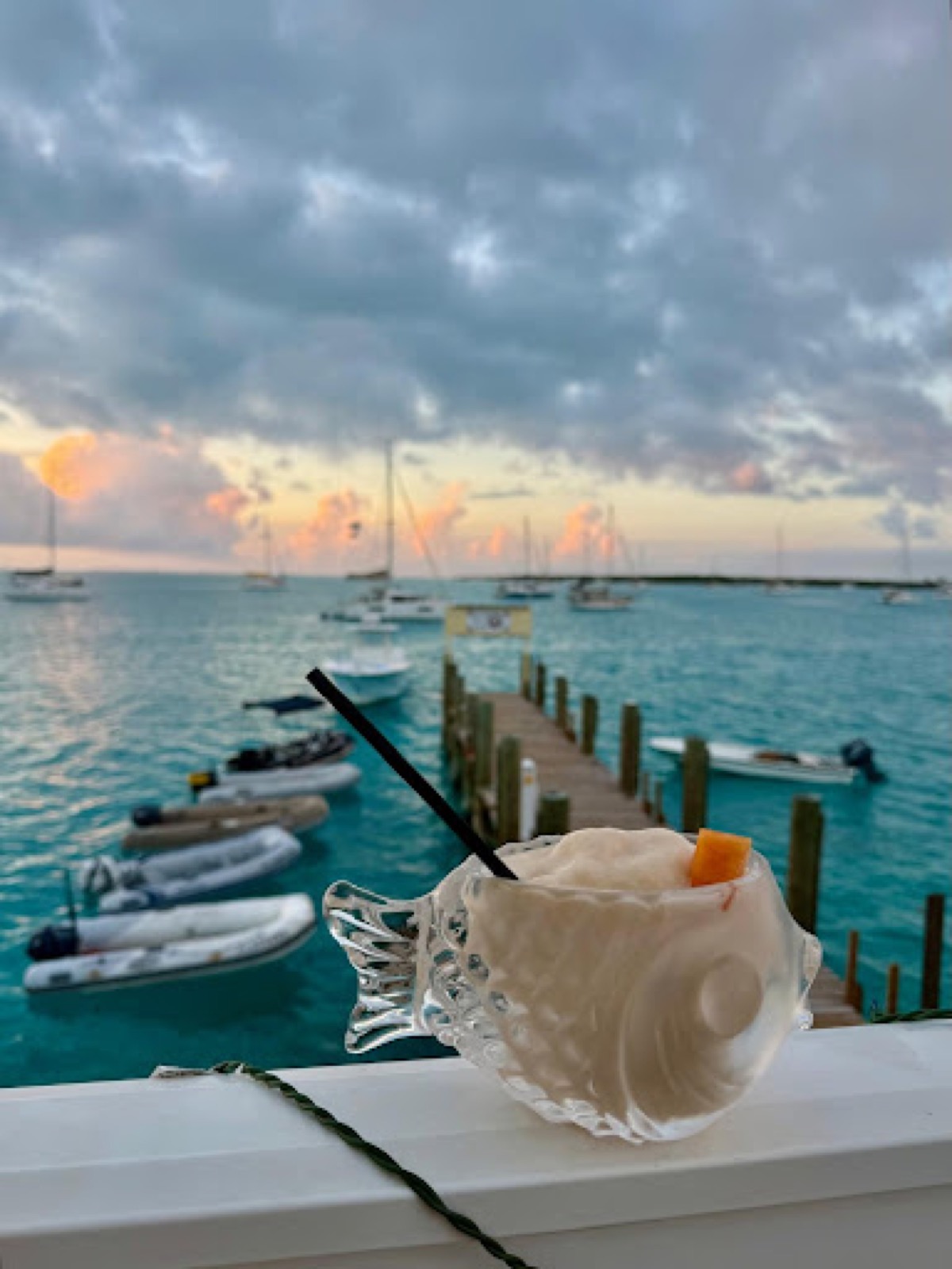 Dinghies tied beside a wooden dock with sailboats anchored beyond at sunset, Black Point
