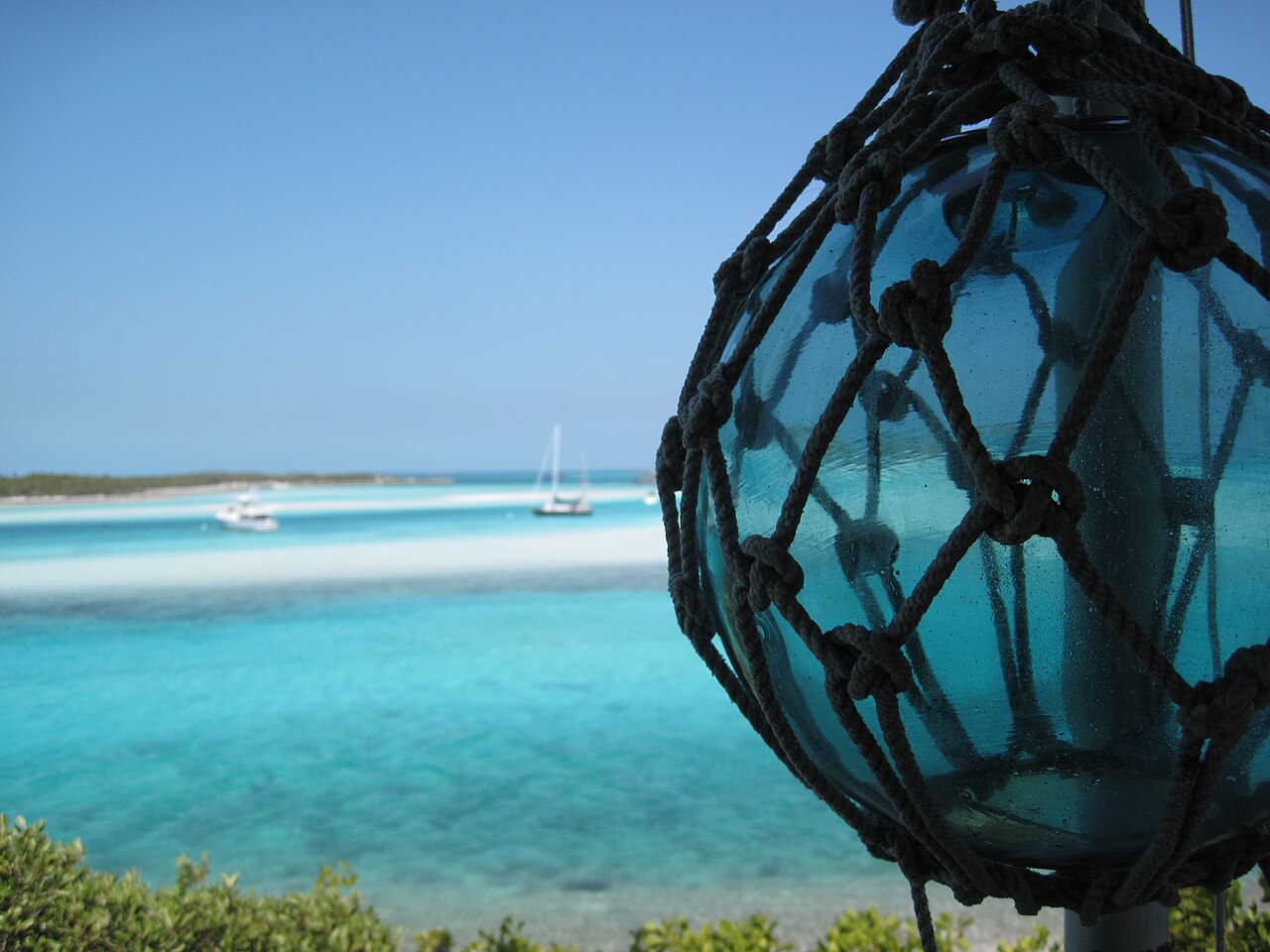 Several boats at anchor in turquoise water off Warderick Wells, with a glass float in the foreground