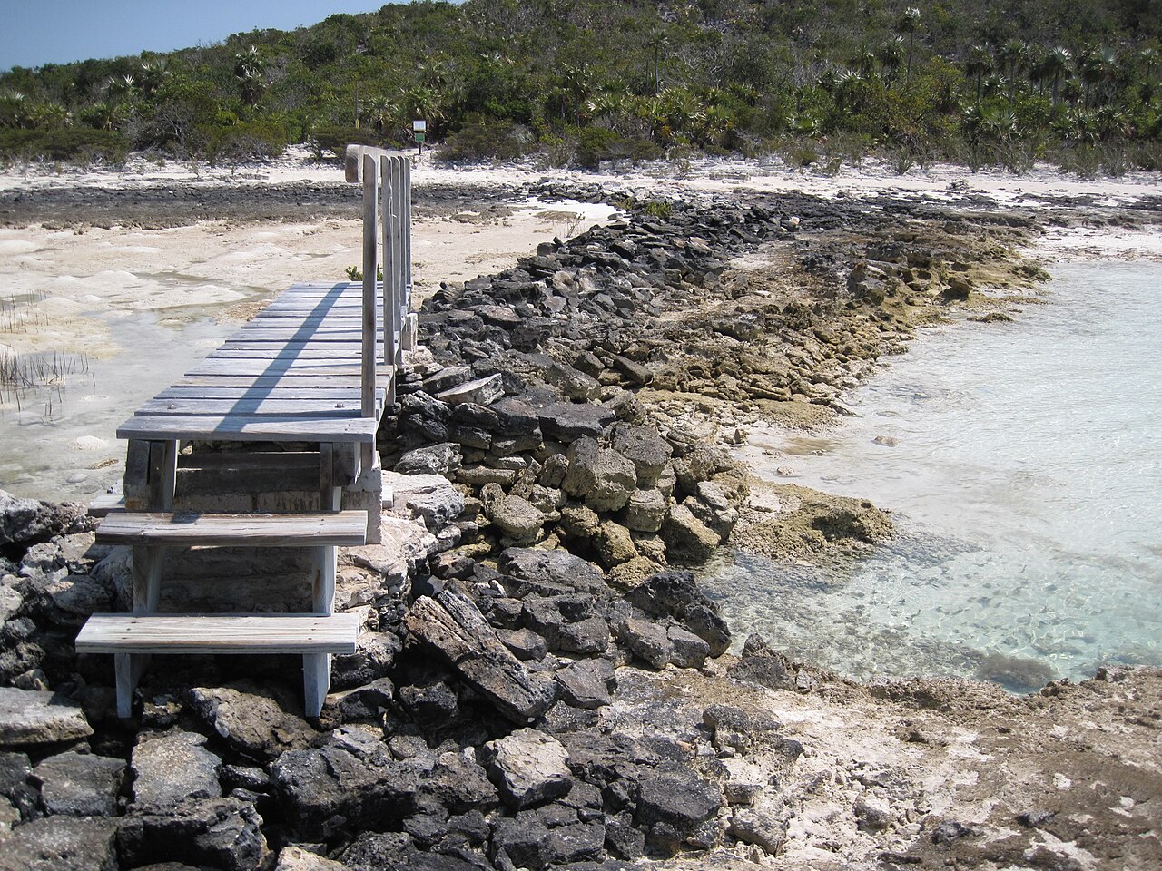A weathered wooden boardwalk and steps running down to the rocky shore at Warderick Wells