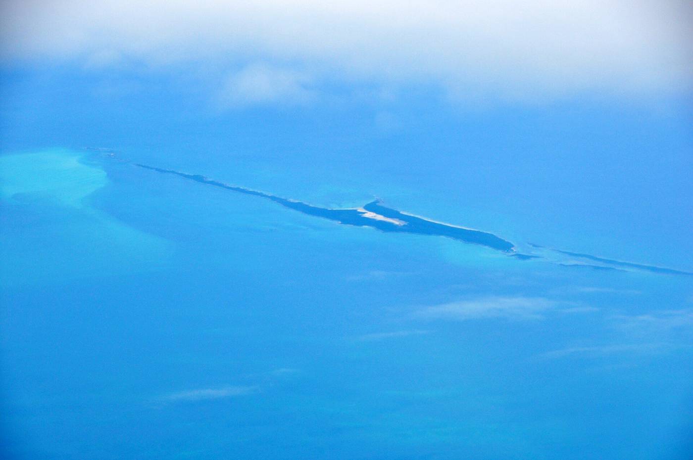 Aerial view of a long narrow cay with reef edges in clear Exuma blue water