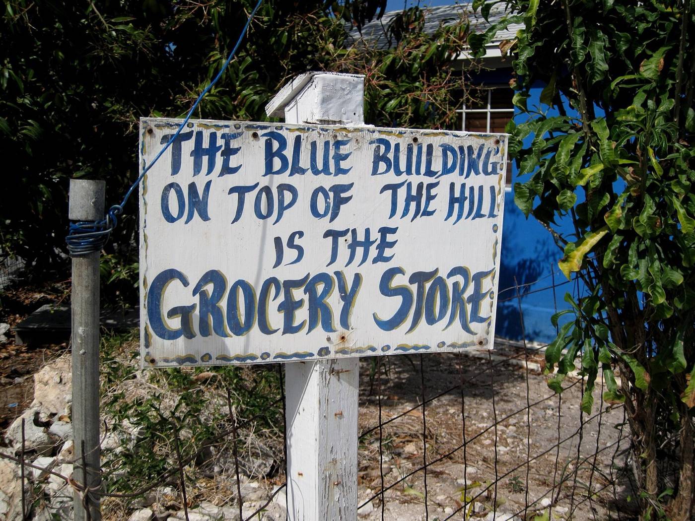 Hand-painted sign on a post: the blue building on the hill is the grocery store