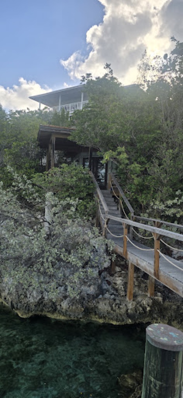 Wooden walkway and steps climbing from the water through trees to a covered deck at Staniel Cay Yacht Club