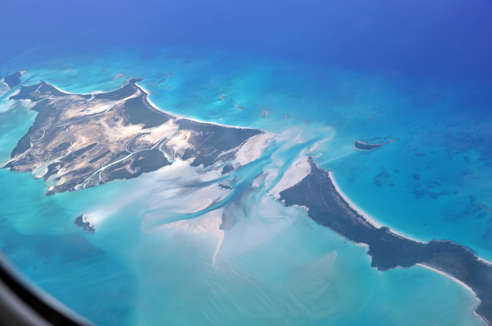 Aerial view of pale tidal channels and sand flats between cays, with turquoise water and dark mangrove islands