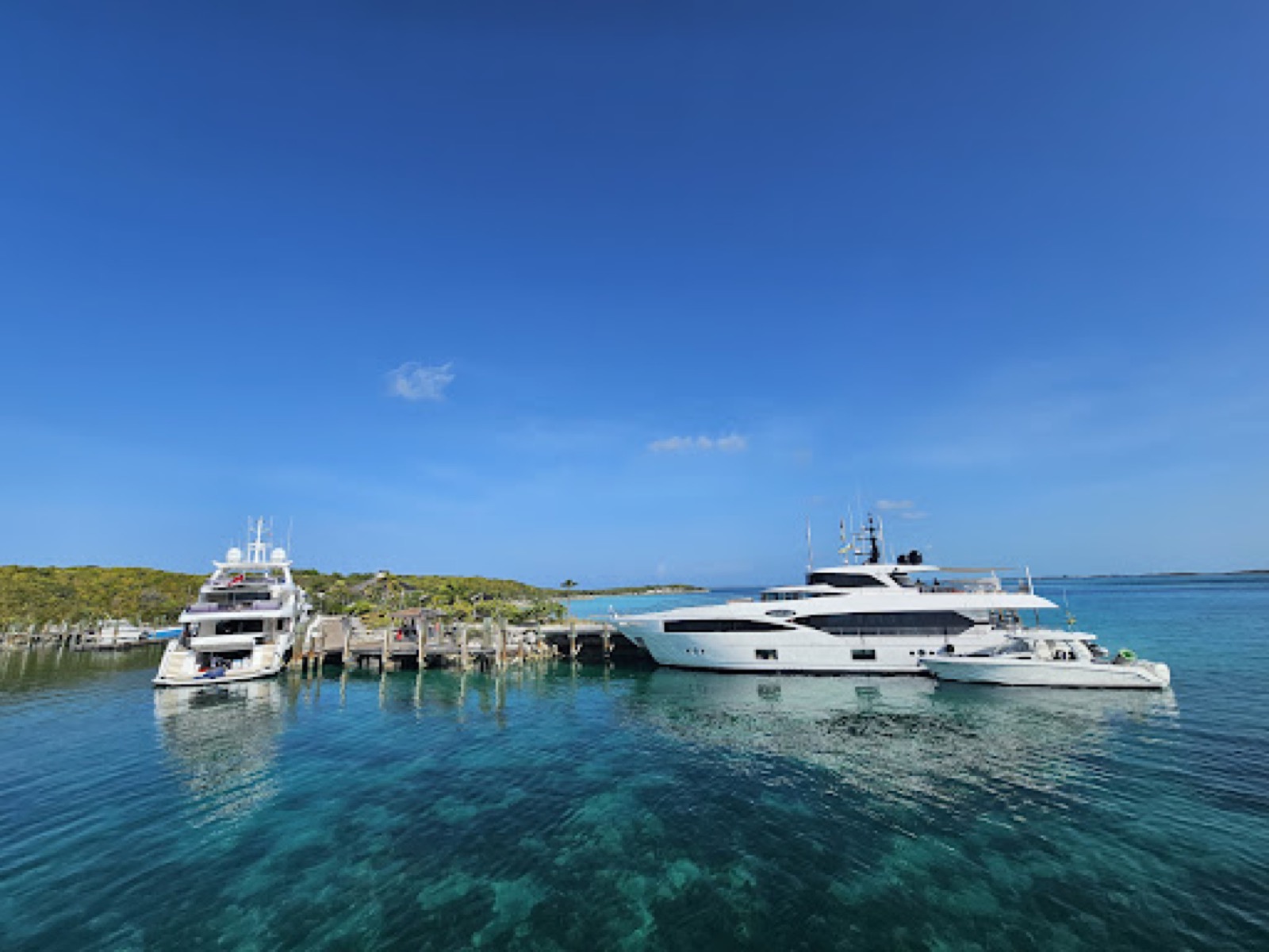 Two large motor yachts moored at a dock on a low, vegetated cay in Highbourne