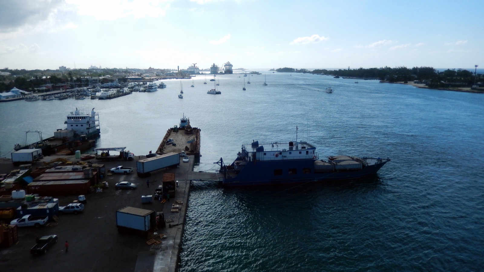Freight vessel moored at the Potter's Cay dock in Nassau, with trucks and containers on the quay and cruise ships in the distance