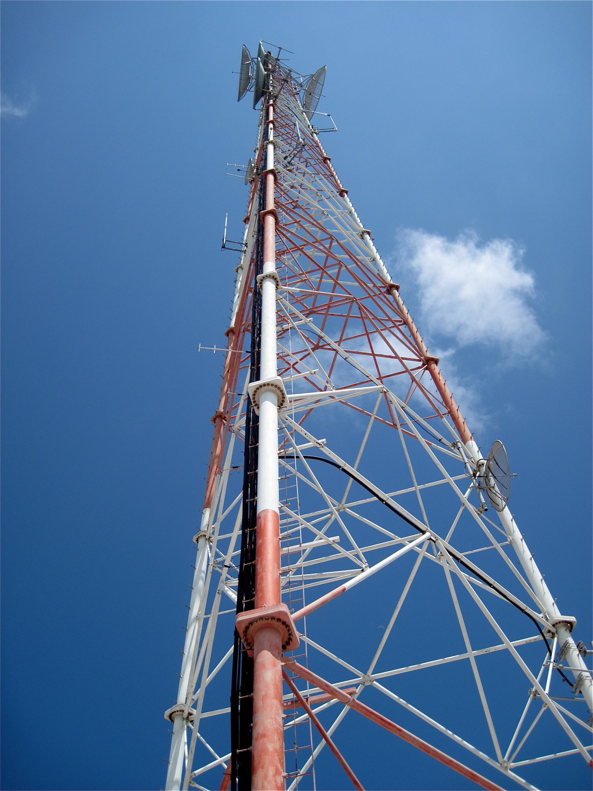 Tall red and white lattice mobile phone tower with dish antennas, photographed against a deep blue sky on Staniel Cay