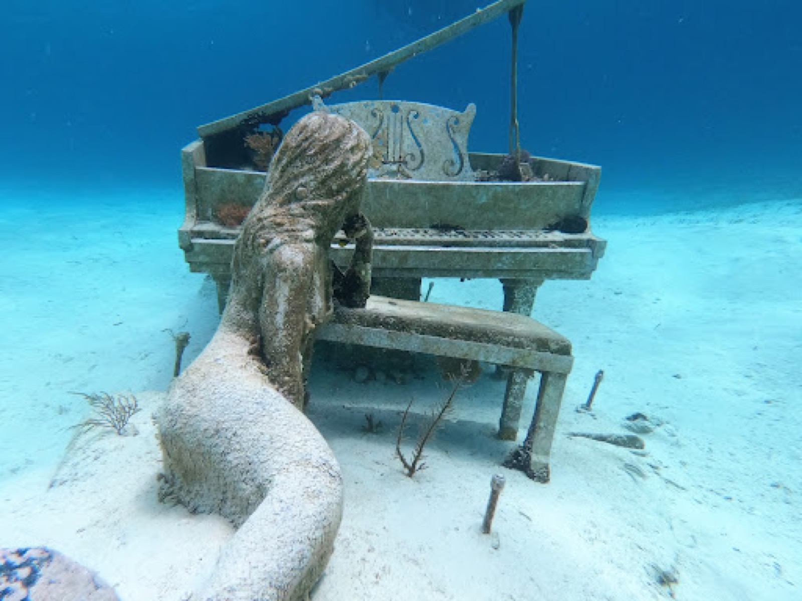 Underwater sculpture of a mermaid at a piano on white sand