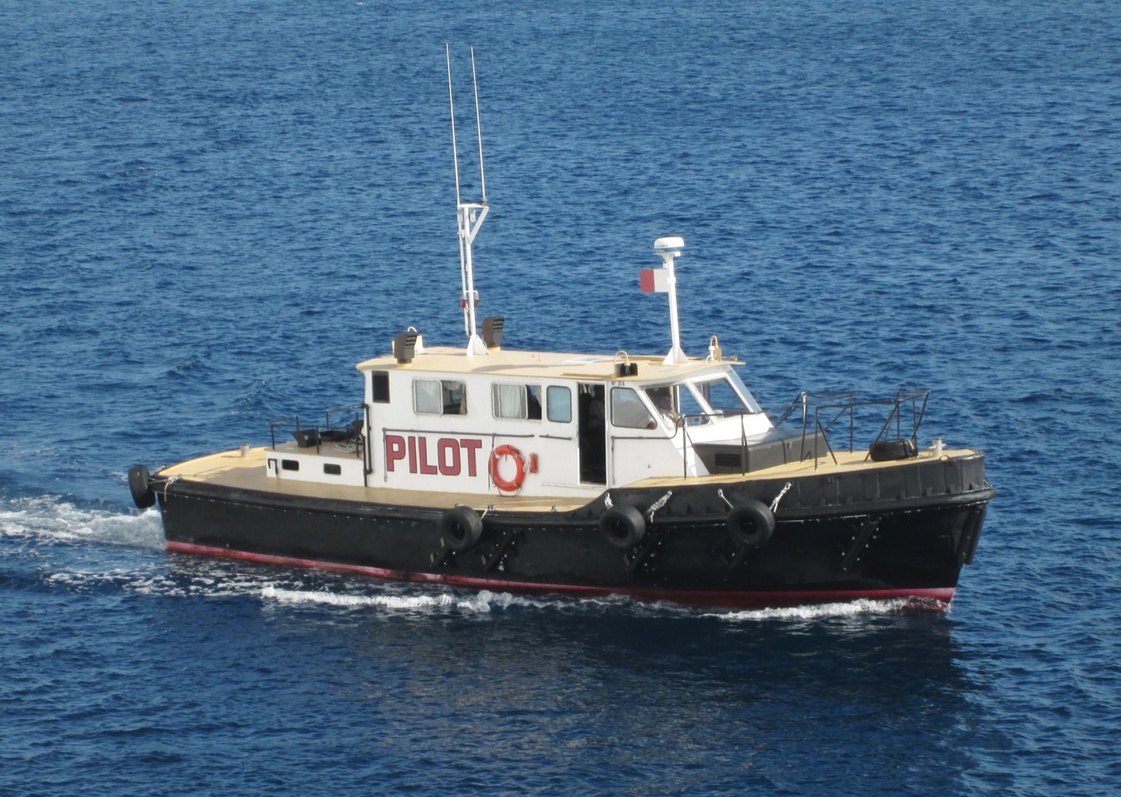 A white and black pilot boat with red trim underway on open blue water