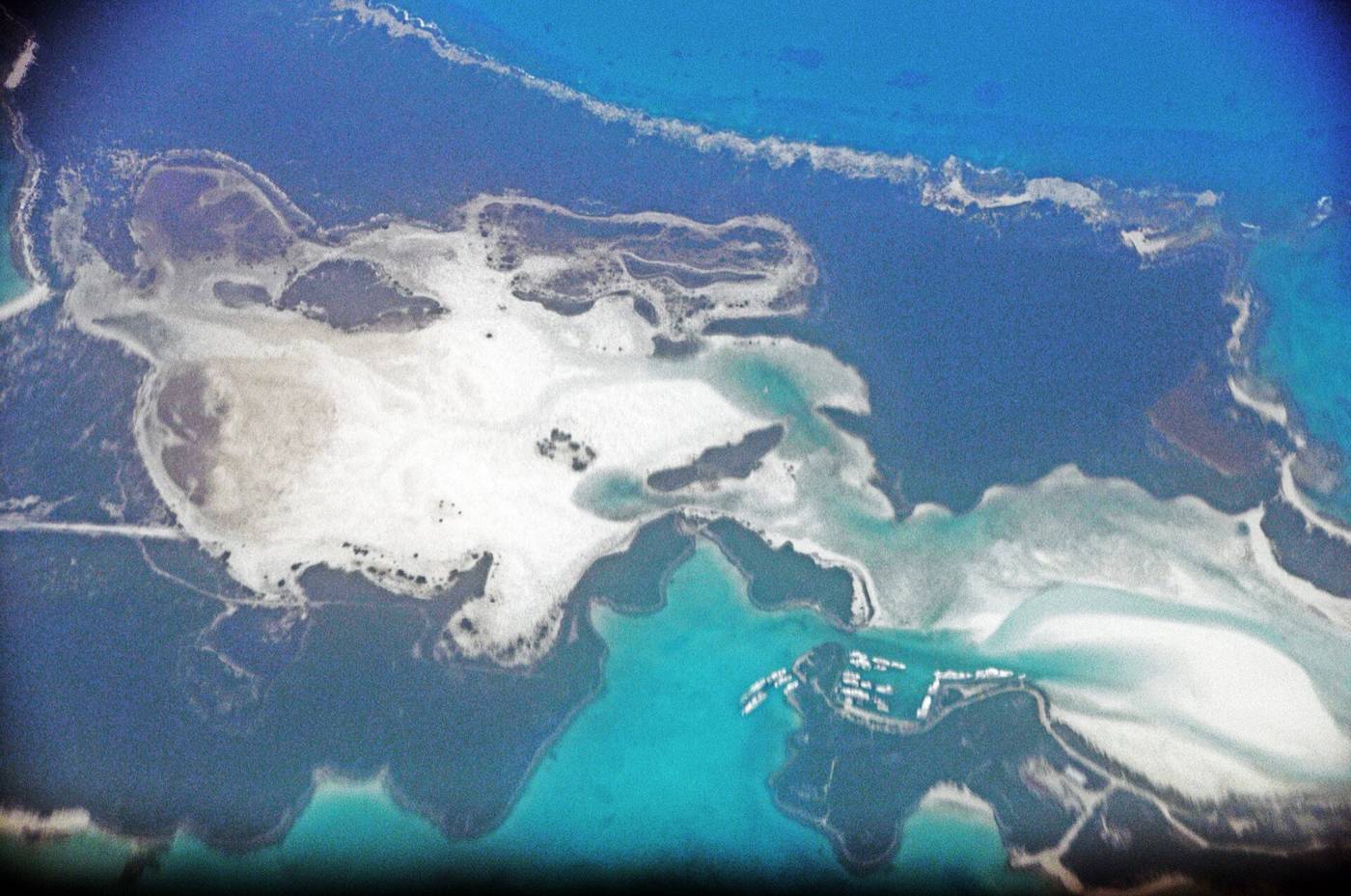 Aerial view of a sandy Exuma cay with a small marina and turquoise channels