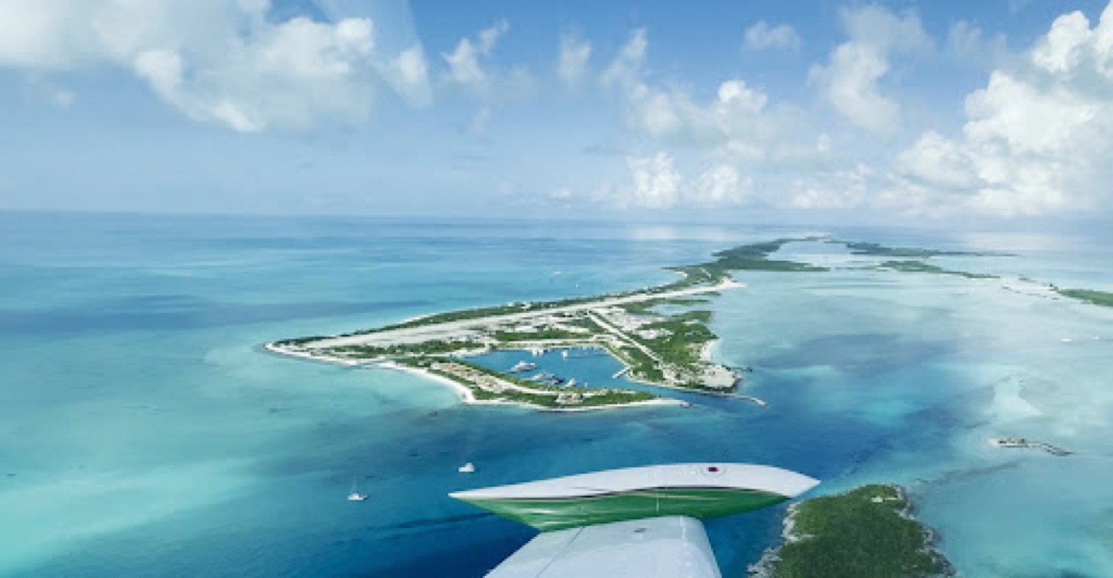 Aerial view of an island with an airstrip and a small marina, seen from a light aircraft wing