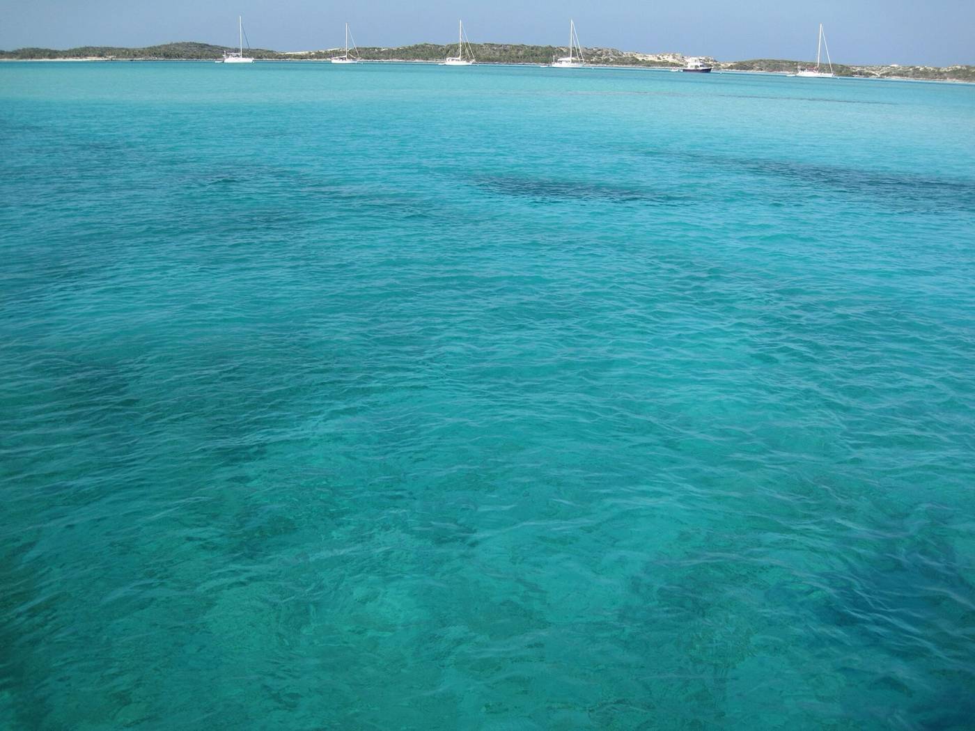 Turquoise water in the foreground with sailboats at anchor on the far shore