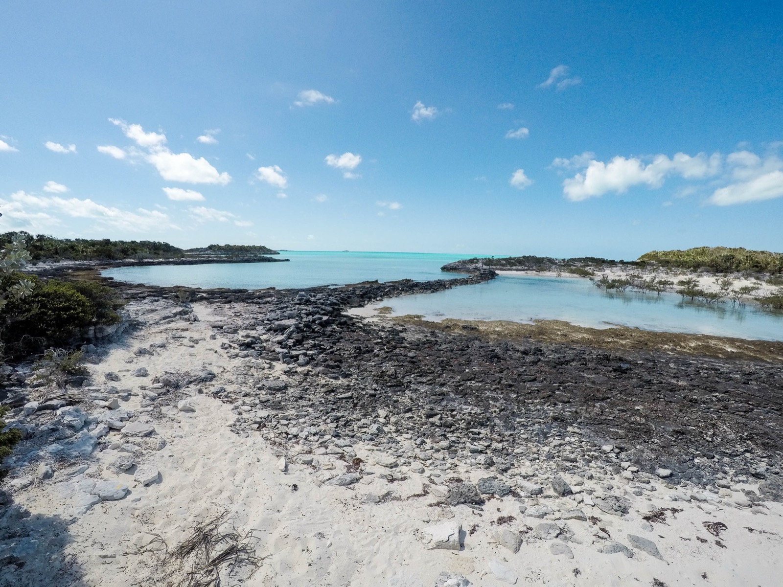Shallow turquoise bay and rocky causeway with sand and mangrove scrub in the Exuma Cays Land and Sea Park