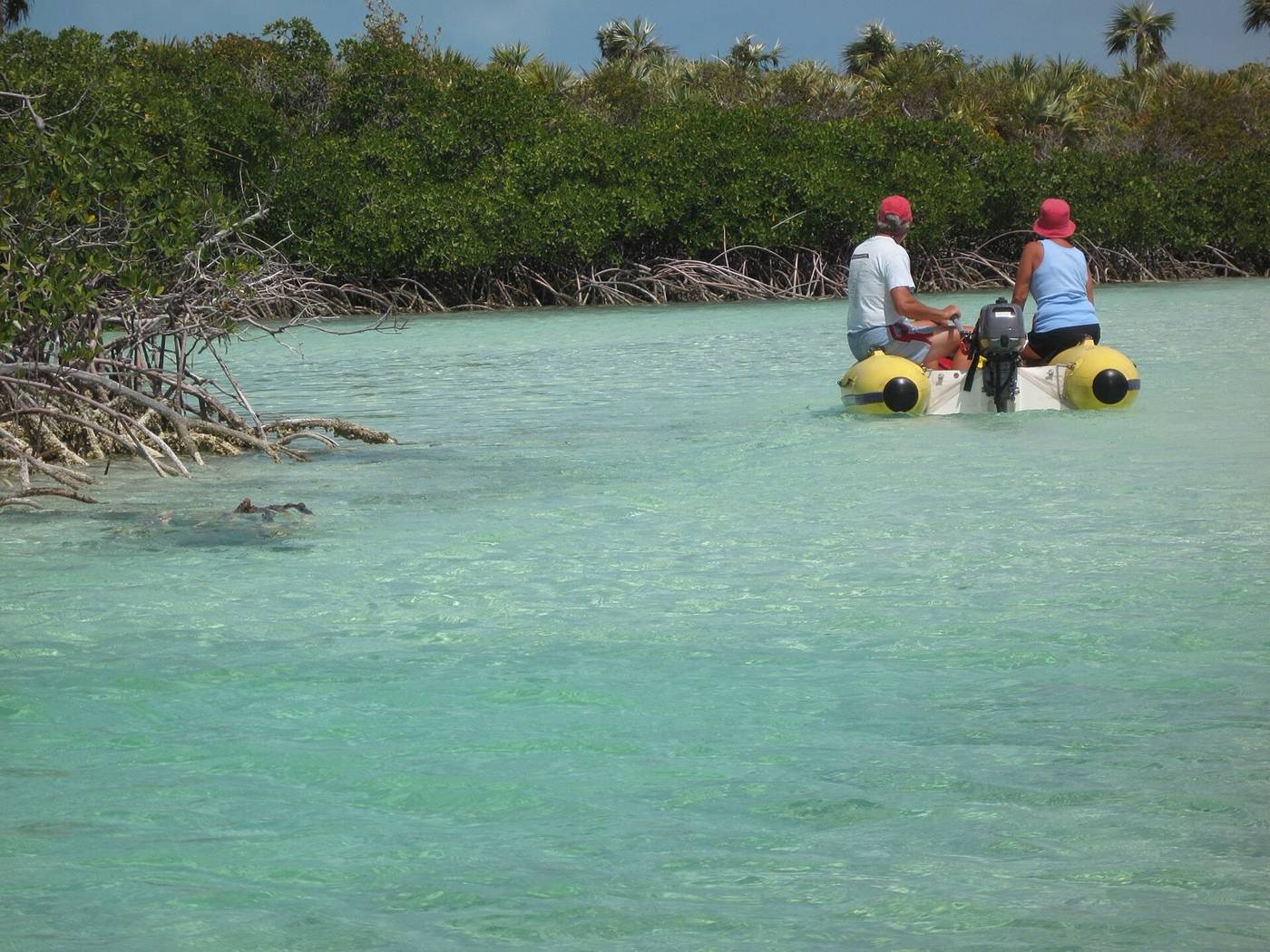 Two people in a yellow inflatable dinghy on a clear mangrove creek in the Exumas