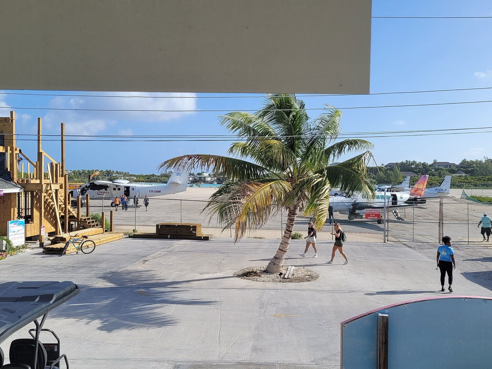 Staniel Cay Airport apron with a Titan Air twin-prop and small aircraft parked beside a palm tree
