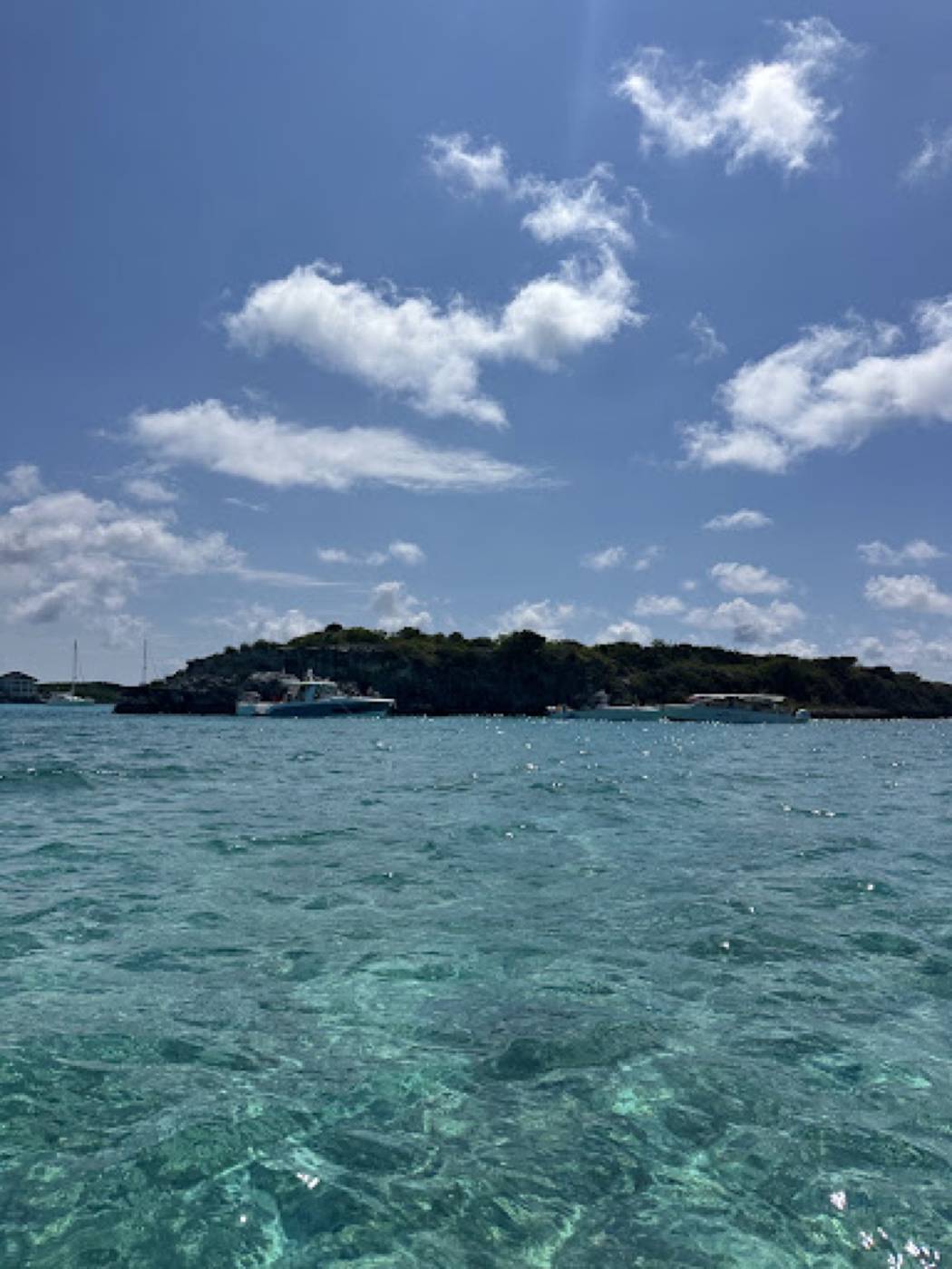 Thunderball Grotto island across turquoise water, tour boats moored along its shore