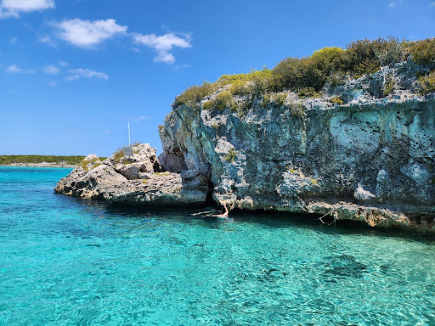Limestone cliff and cave mouth at the water line beside clear turquoise water