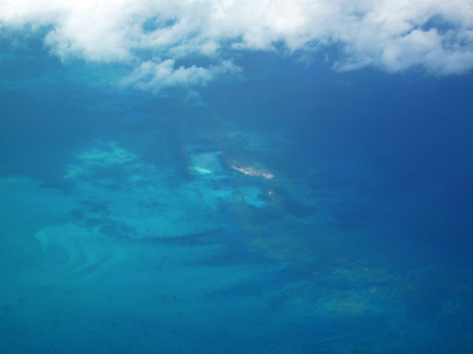 Aerial view of a long, narrow cay surrounded by pale blue shallows in the Northern Exuma Islands