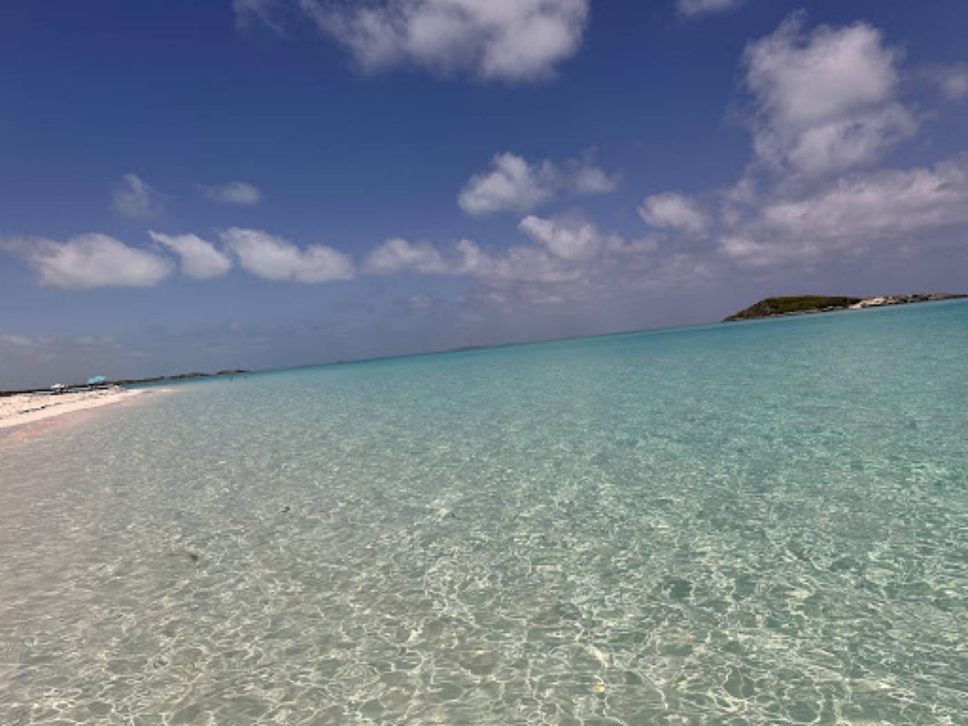 Clear, shallow turquoise water over sand along a white beach, with an island on the horizon