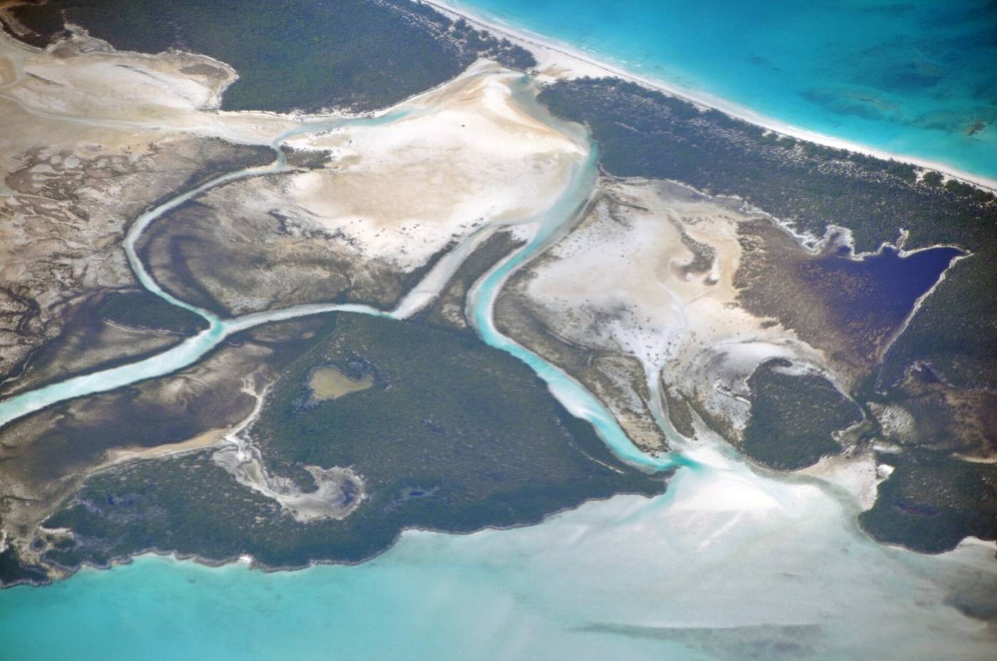 Aerial view of pale sand banks and tidal channels with turquoise shallows and dark cays