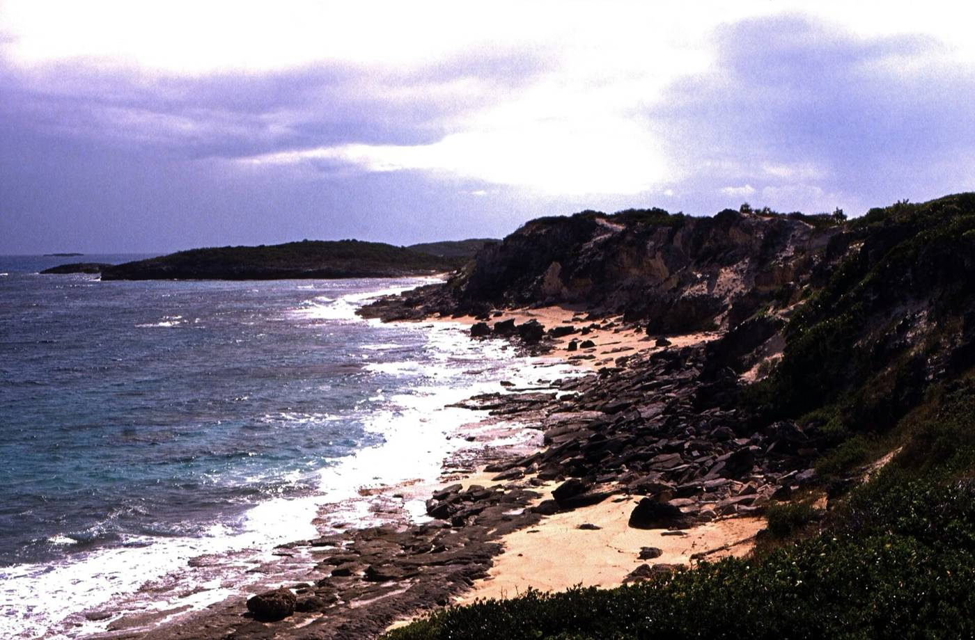 Rocky shoreline and pale sand under a stormy sky on Great Exuma's Stocking Island