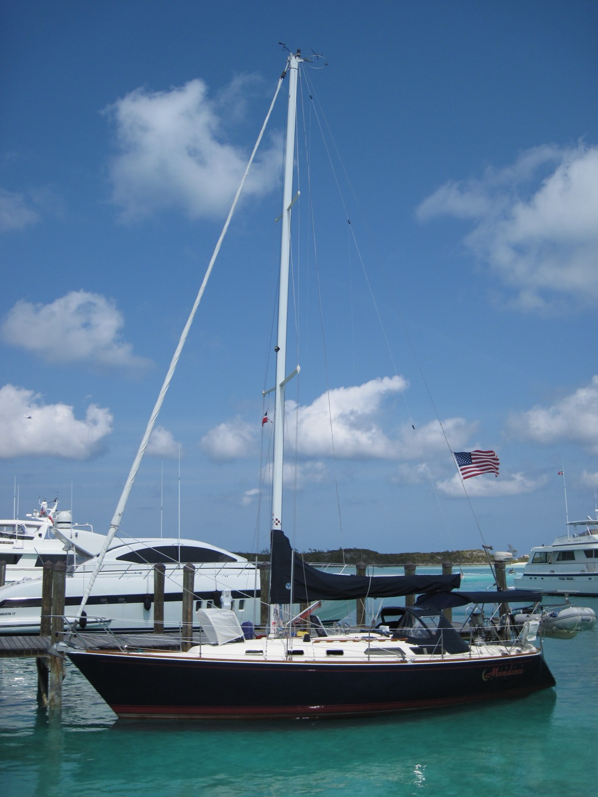 Dark-hulled sailboat tied at a dock beside white motor yachts in a Bahamas marina